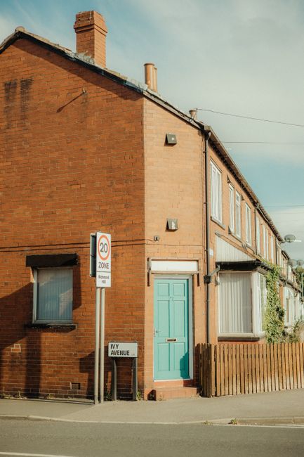 Photograph of a two-story residential house with red brick walls and a sloped tiled roof, situated on Yarningale Road. The house features white-framed windows, some with window security bars, and a bl